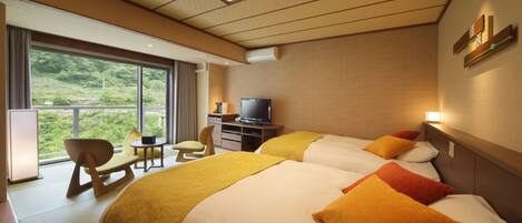A hotel room with two beds, a TV, a desk, and a view of greenery outside.