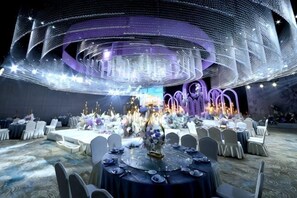 A banquet hall with round tables, chairs, and a central stage with floral arrangements. - Yulin Hotel (Yulin)