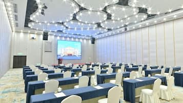 Un salón de conferencias con filas de mesas, sillas, una pantalla grande y un proyector.
