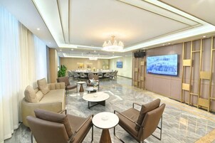 A hotel lobby with a seating area, a television screen, and a conference room in the background.