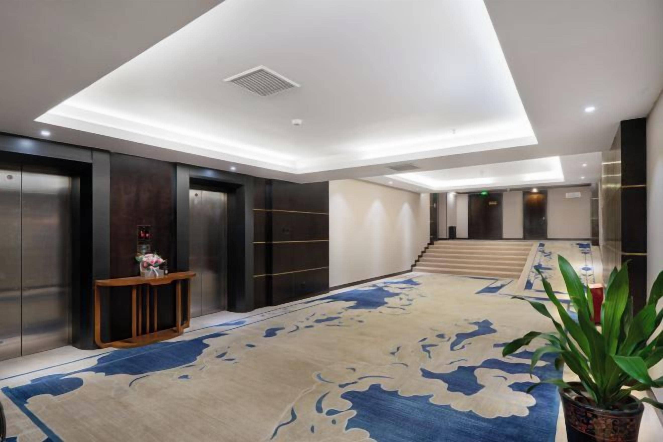 Un hall de hotel con piso alfombrado, una recepción y una escalera que conduce a los pisos superiores.