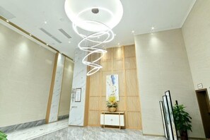 A modern hotel lobby with a marble floor, a spiral light fixture, a reception desk, and a large painting on the wall. - Yulin Hotel (Yulin)