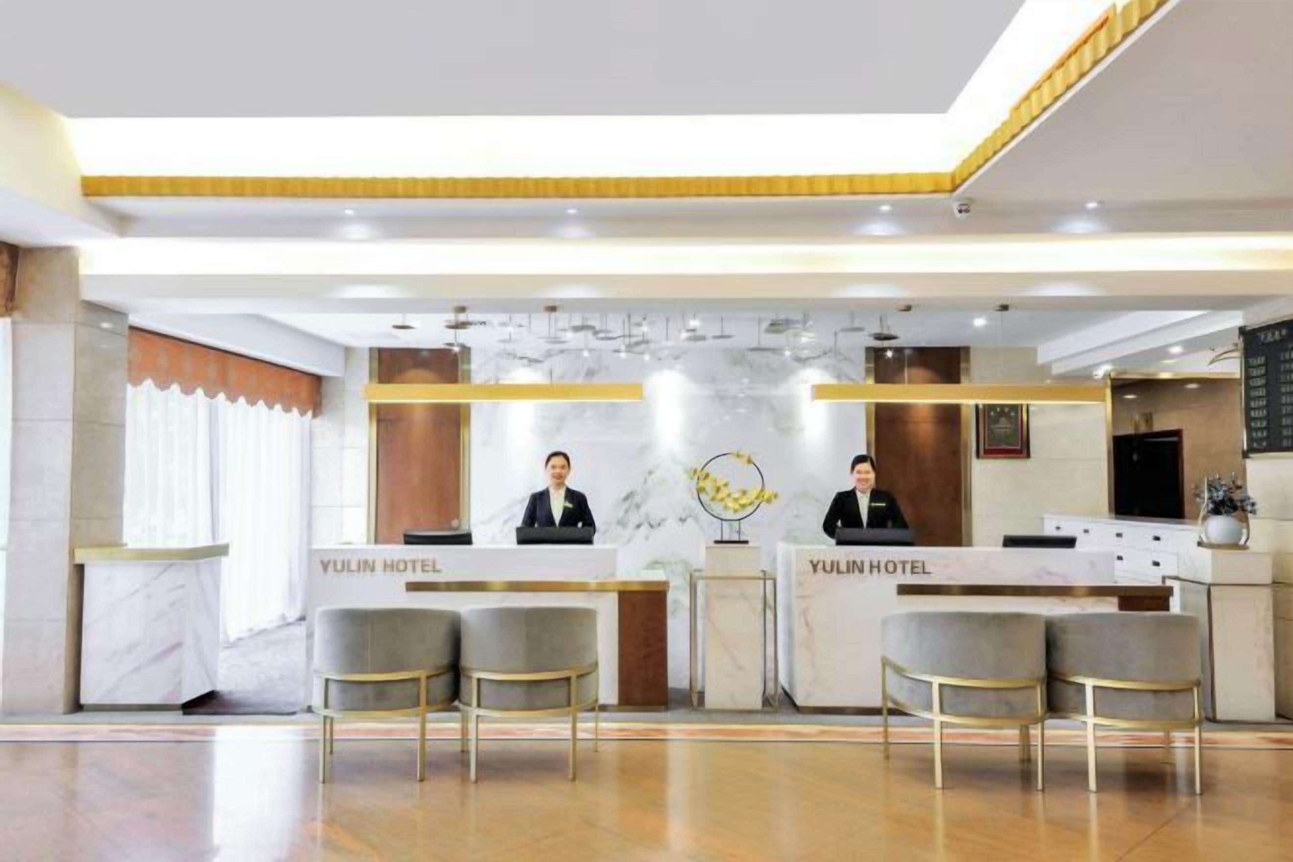 A reception area with a marble counter, two receptionists, and a modern chandelier.
