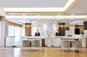 A reception area with a marble counter, two receptionists, and a modern chandelier.