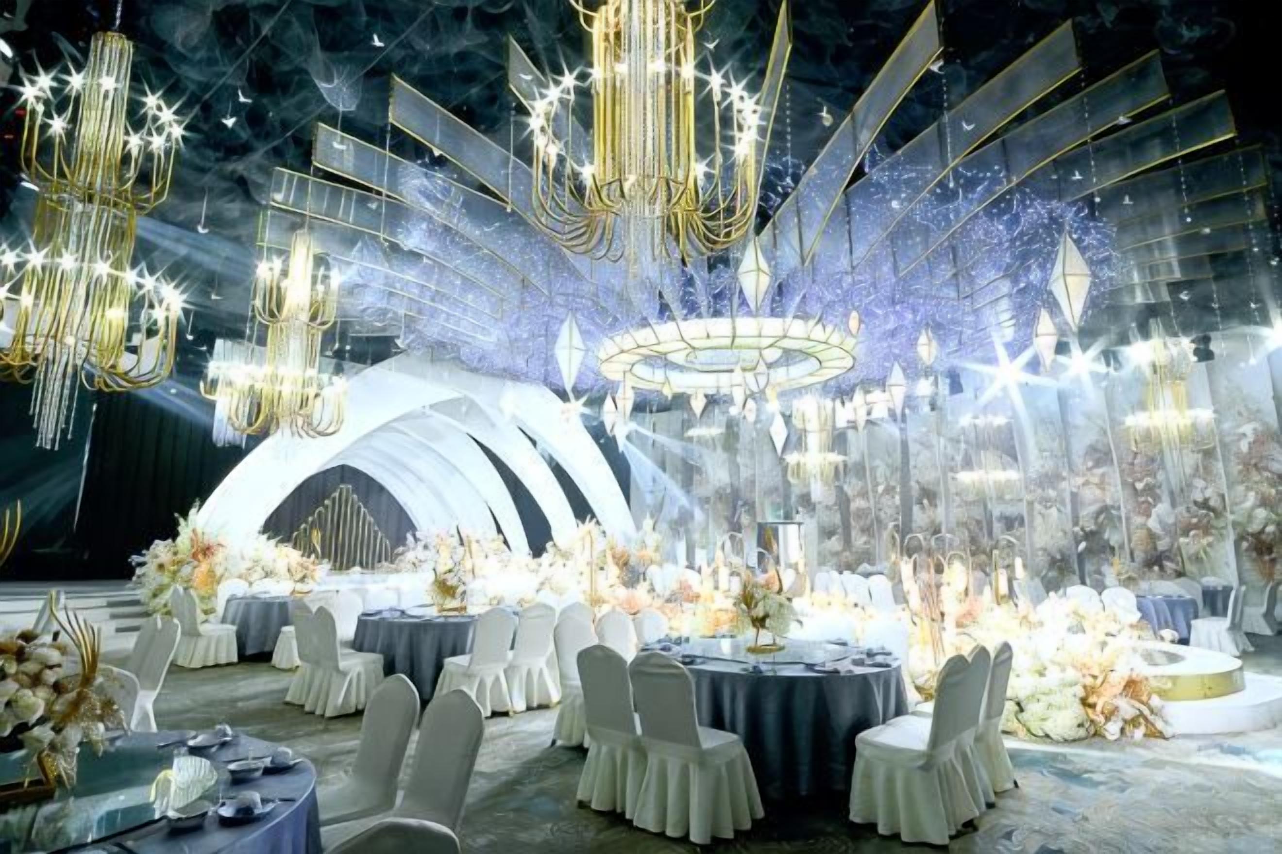 A formal event space with round tables, chairs, and elaborate chandeliers.