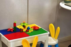 A white table with a LEGO play mat and a toy chair with yellow and blue details. - Yulin Hotel (Yulin)