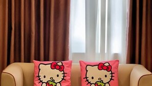 Two Hello Kitty cushions on a beige sofa against a window with brown curtains. - Yulin Hotel (Yulin)