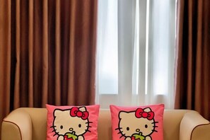 Due cuscini di Hello Kitty su un divano beige, davanti a una finestra con tende marroni.