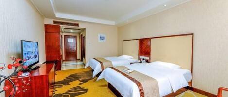 A hotel room with two beds, a desk with a television, and a carpet with a floral pattern.