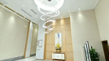 A hotel lobby with a marble floor, a modern spiral light fixture, a reception desk, and a potted plant.