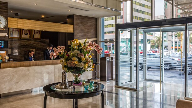 Un hall d’hôtel comprenant un comptoir d’accueil, une grande fenêtre donnant sur la rue et une table ronde agrémentée d’un arrangement floral.