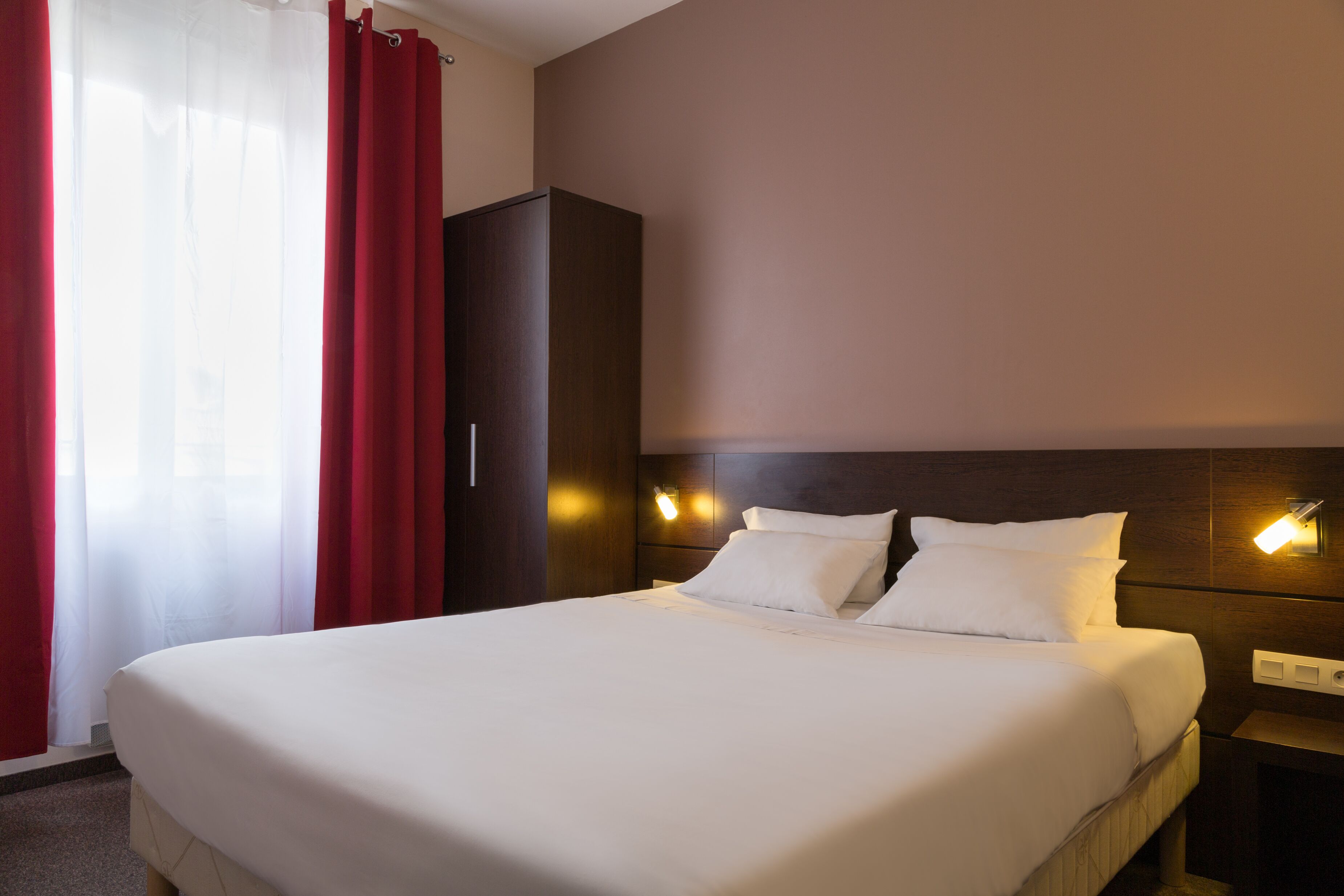 Une chambre d’hôtel avec un grand lit, une armoire et des lampes fixées au mur.