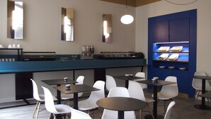 A modern cafe with a long counter, white chairs, and a blue wall with shelves. - Urban Style Hotellerie du Cheval Noir (Saint-Etienne)