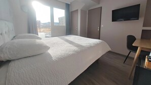 A hotel room with a large bed, a desk, a chair, a TV, and a sliding door to a balcony. - Urban Style Hotellerie du Cheval Noir (Saint-Etienne)