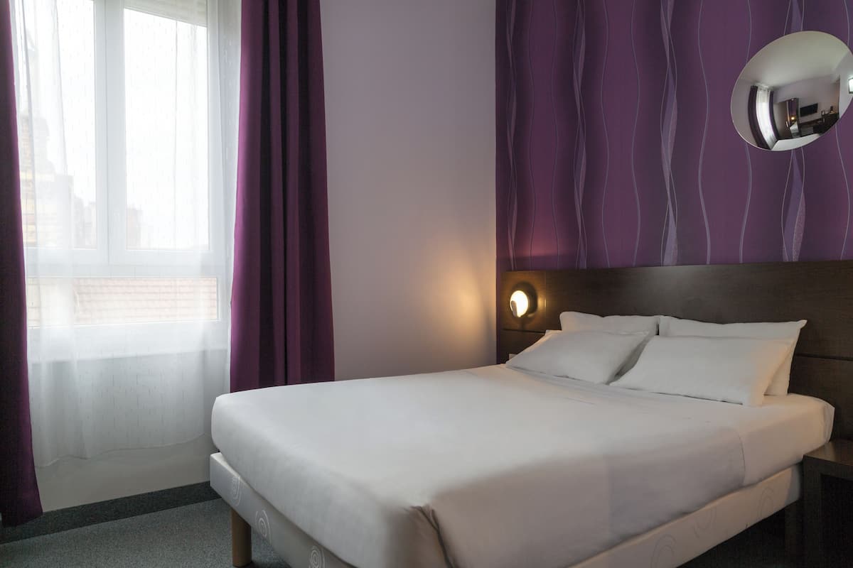 A neatly made bed in a hotel room with a headboard, a bedside table, and a wall-mounted mirror.