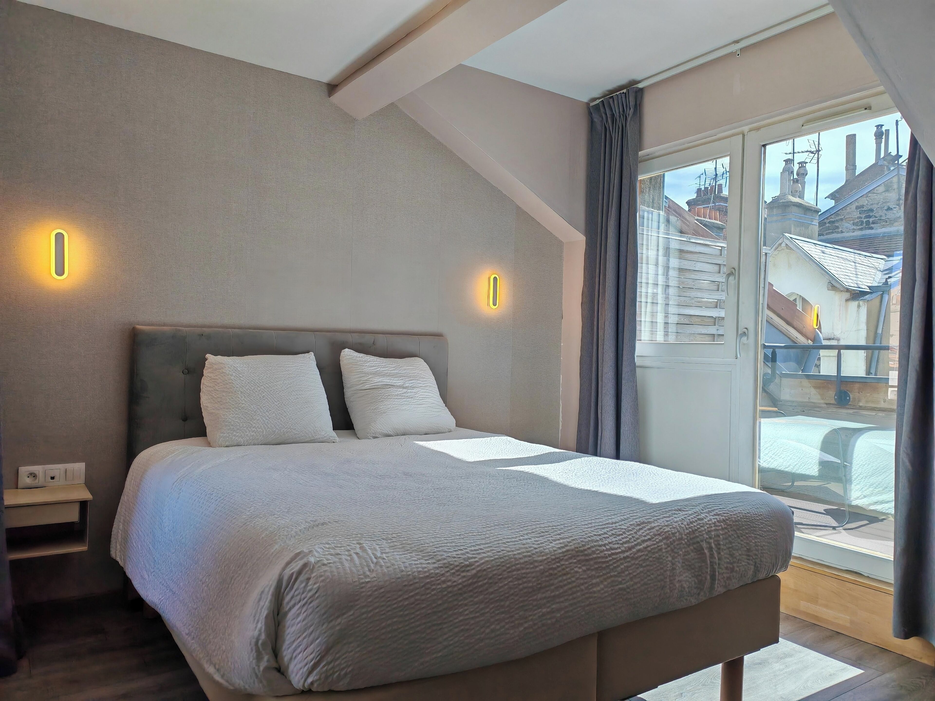 A bedroom with a large bed, two bedside lamps, and a view of the outside through a window.