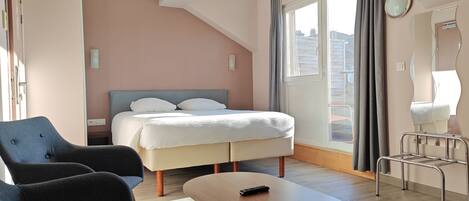 A modern hotel room with a bed, two armchairs, a small table, and a window with curtains.
