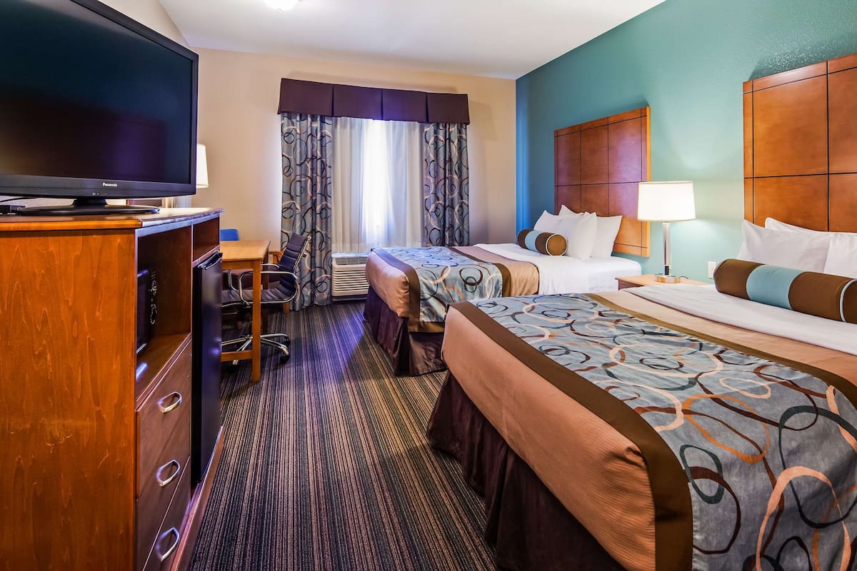 A hotel room with two beds, a desk with a chair, a television, and a window with curtains.