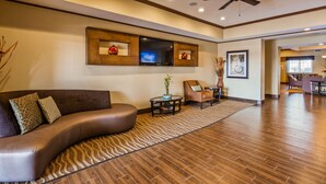 A modern living room with a curved sofa, a coffee table, and a television mounted on the wall. - Best Western Plus Seminole Hotel & Suites (Seminole)