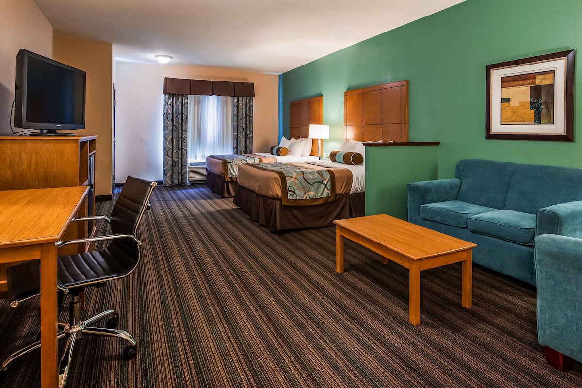 A hotel room with a bed, a blue sofa, a wooden table, a TV, and a desk with chairs.