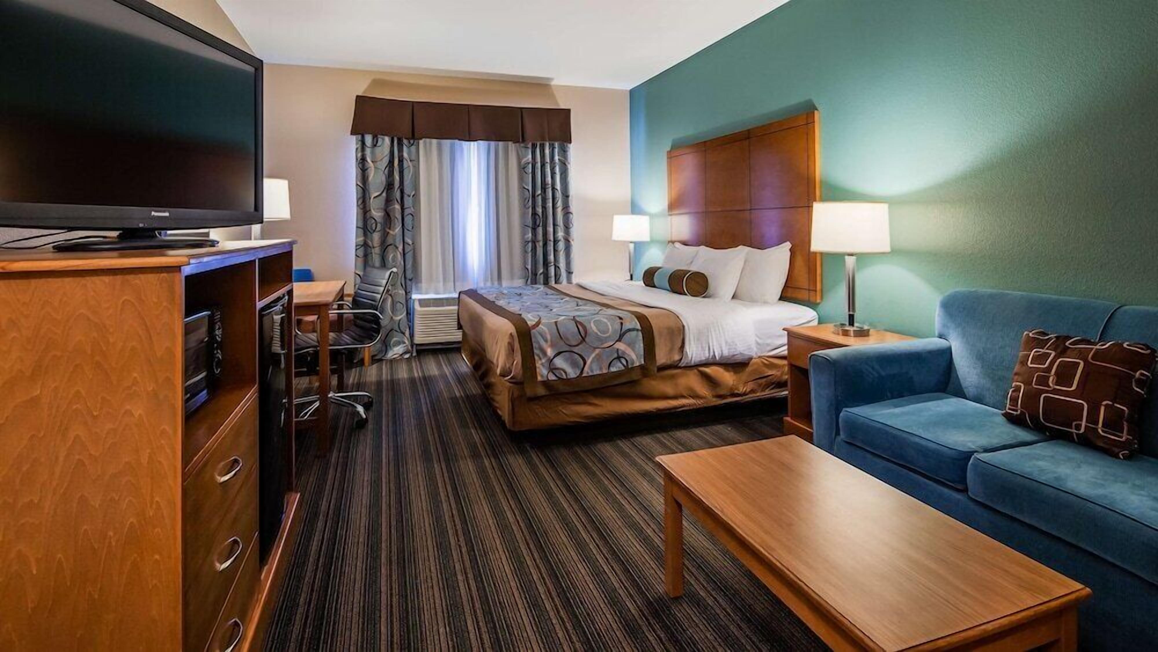 A hotel room with a bed, a desk, a television, a sofa, and a lamp.