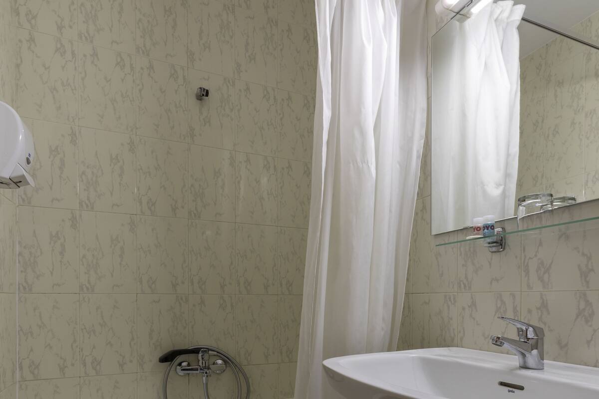 A bathroom with a bathtub, a sink, a glass shelf with toiletries, and a shower curtain.