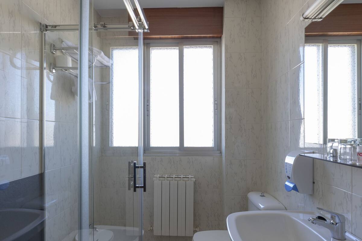 A bathroom with a glass shower enclosure, a toilet, and a sink.