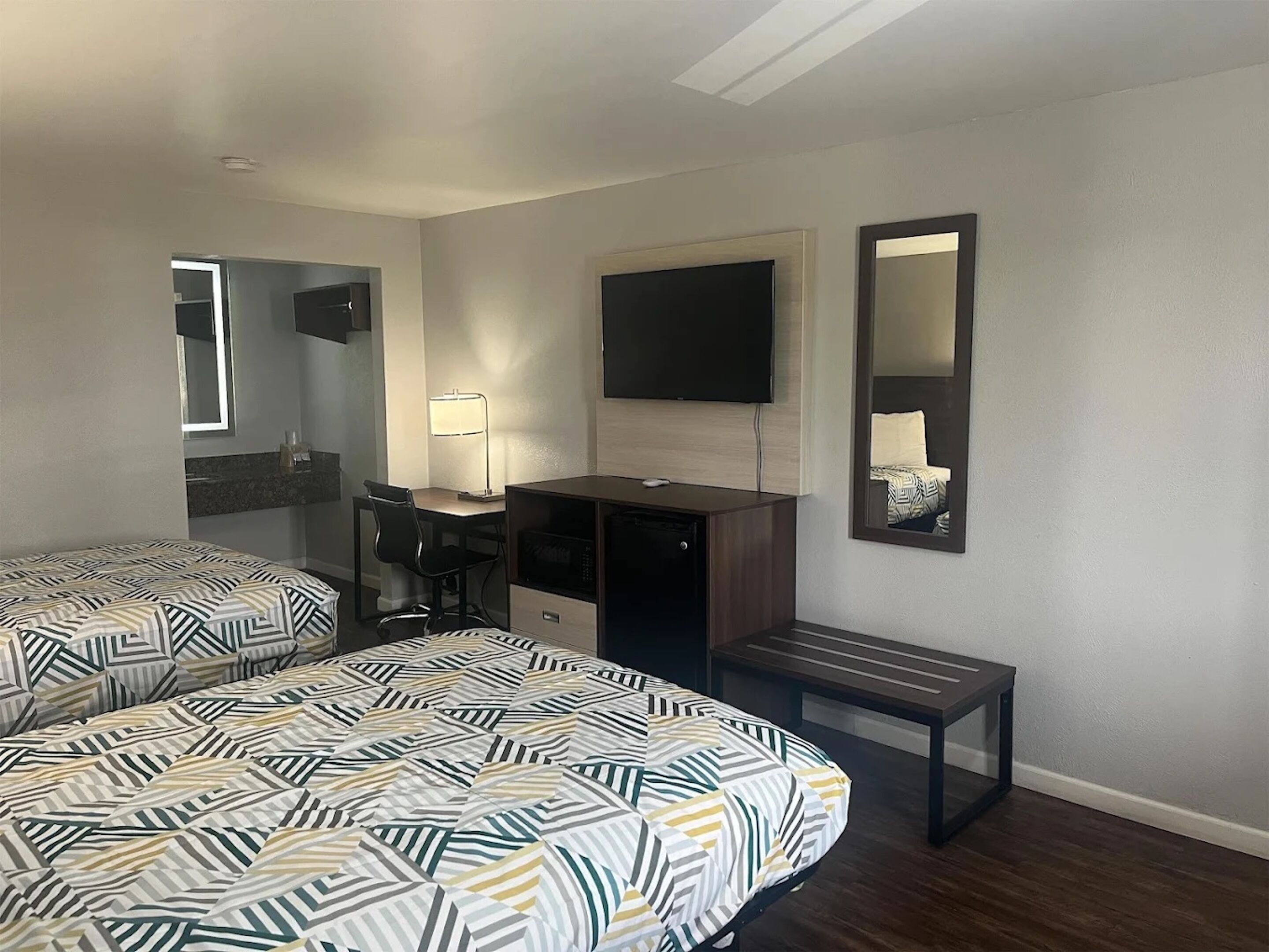 A hotel room with two beds, a desk, a chair, a TV, and a mirror.