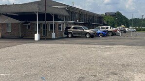 A parking lot with several cars, a building with a flat roof, and a sign in the background. - Motel 6 Saint George, SC – I-95 (St. George)
