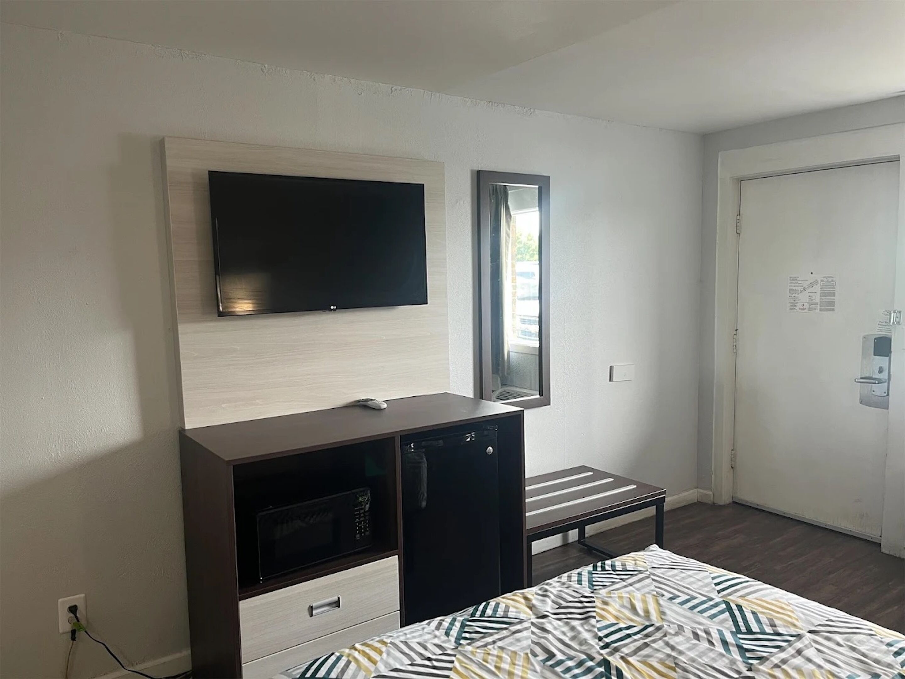 A hotel room with a flat-screen TV mounted on the wall, a small table, a microwave, and a bed with striped bedding.