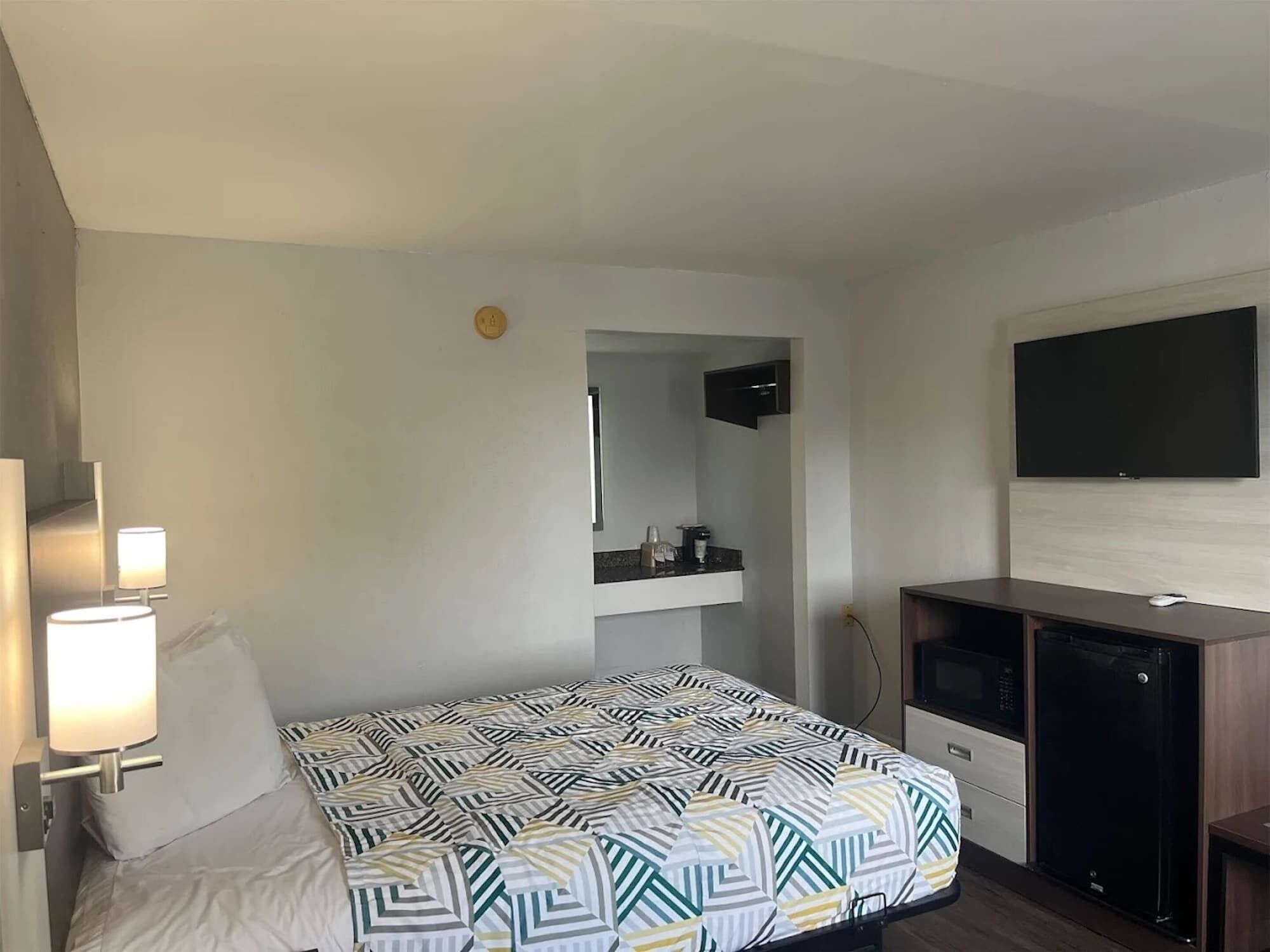 A hotel room with a bed, a desk, a TV, and a minibar.