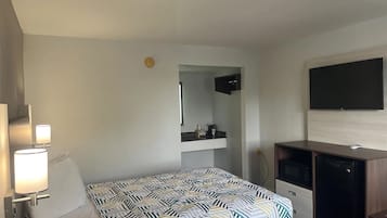 A hotel room with a bed, a desk, a TV, and a minibar.