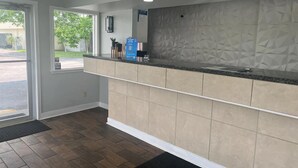 A reception area with a counter, a door leading outside, and a patterned wall. - Motel 6 Saint George, SC – I-95 (St. George)