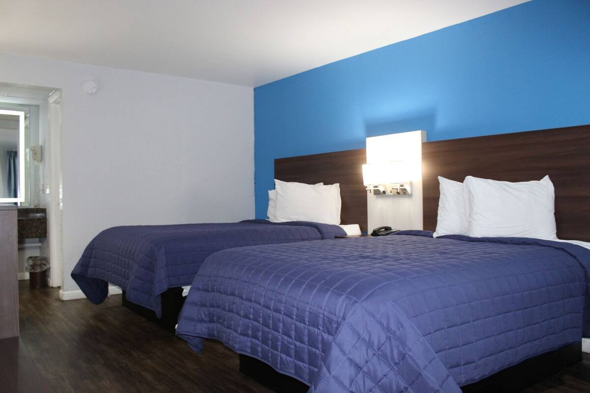 A hotel room with two beds, each with a blue quilted bedspread and white pillows.