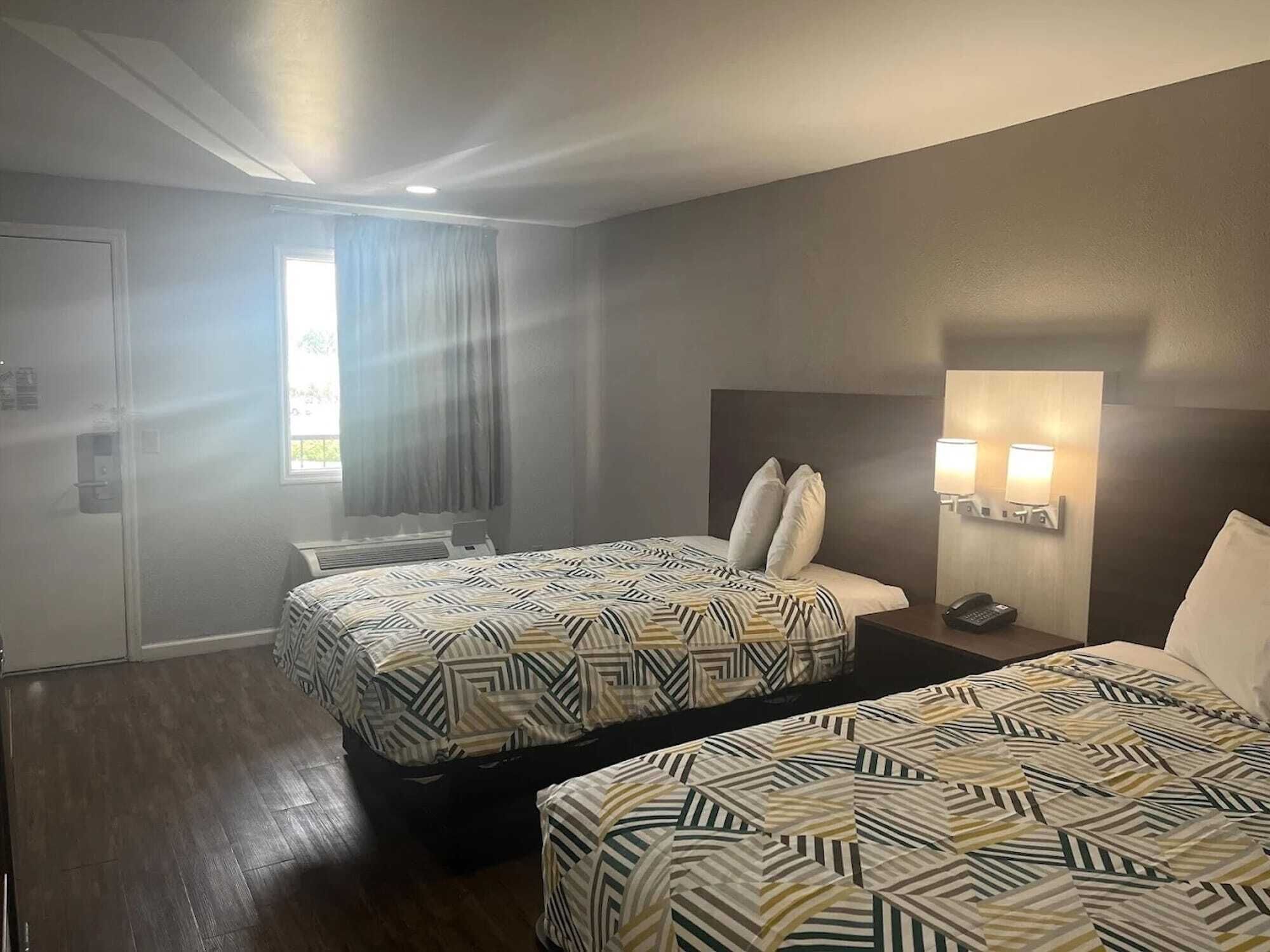 Een hotelkamer met twee bedden, een raam met gordijnen, een wandlamp en een telefoon op het nachtkastje.