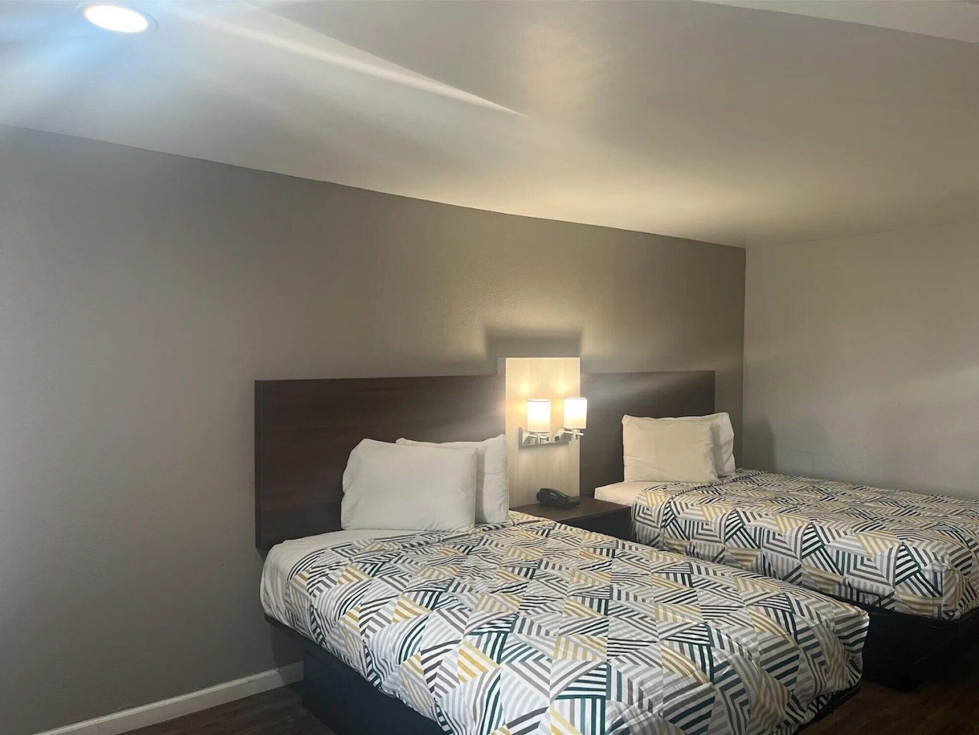A hotel room with two beds, each with patterned bedding, a dark headboard, and a wall-mounted light fixture.