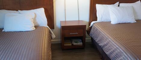 A hotel room with two beds, each with white linens, a wooden nightstand with a drawer, and two wall-mounted lamps.