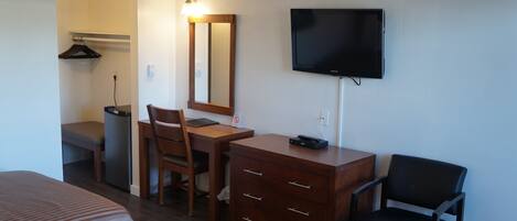 A hotel room with a bed, a desk with a chair, a dresser, a television, and a mirror.