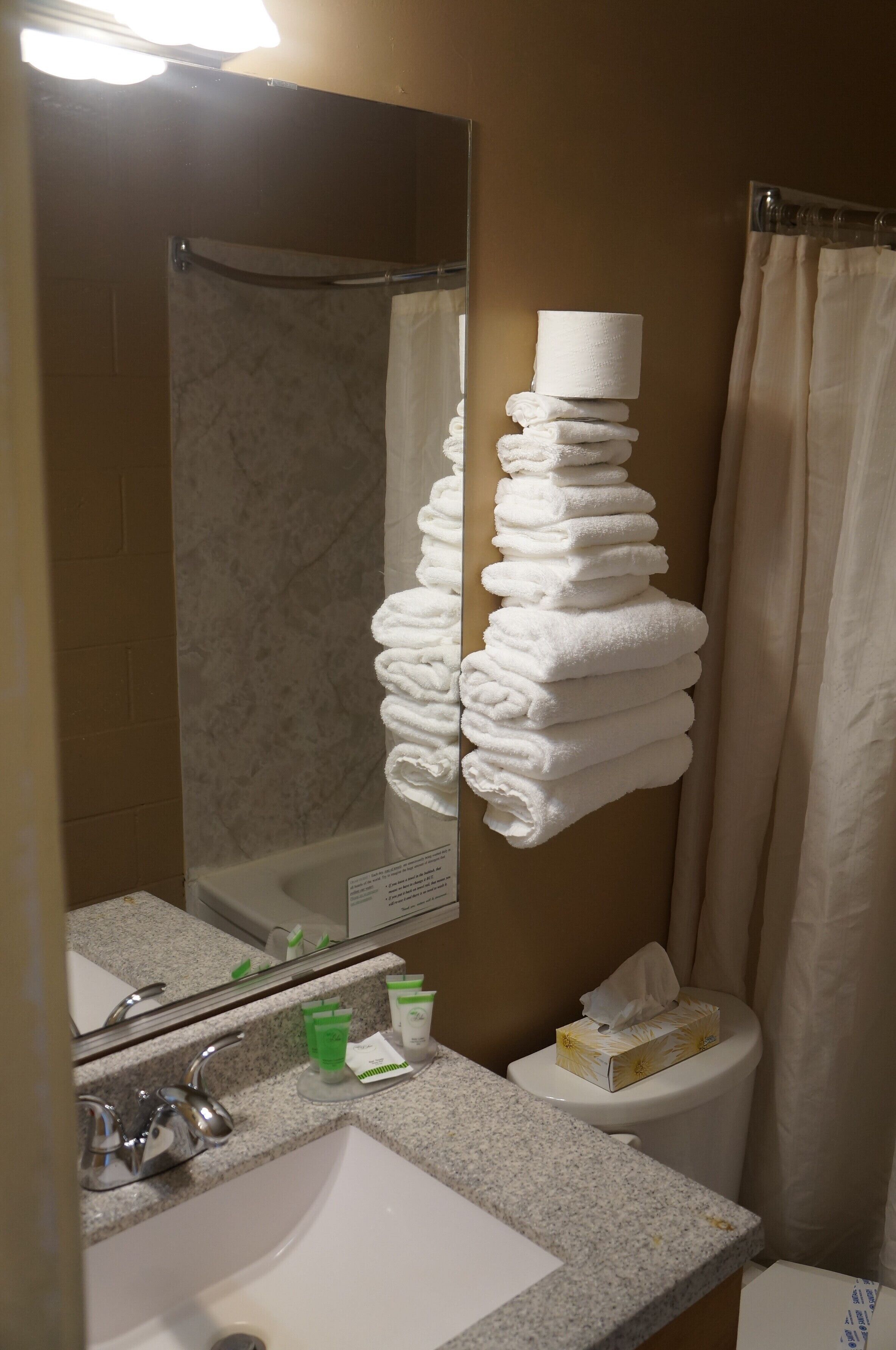 A bathroom with a sink, mirror, and stacked towels.