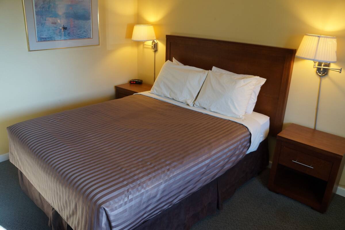 Una cama bien hecha con un edredón marrón a rayas, dos mesitas de noche con lámparas y un cuadro en la pared.