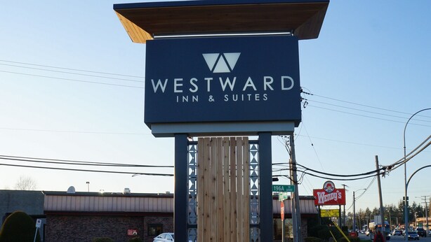 Letrero de Westward Inn & Suites, con una estructura de madera y un cielo azul despejado al fondo.
