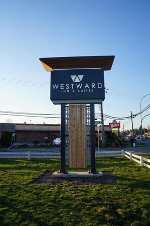 A Westward Inn & Suites sign with a wooden structure and a clear blue sky in the background. - Westward Inn & Suites (Langley)