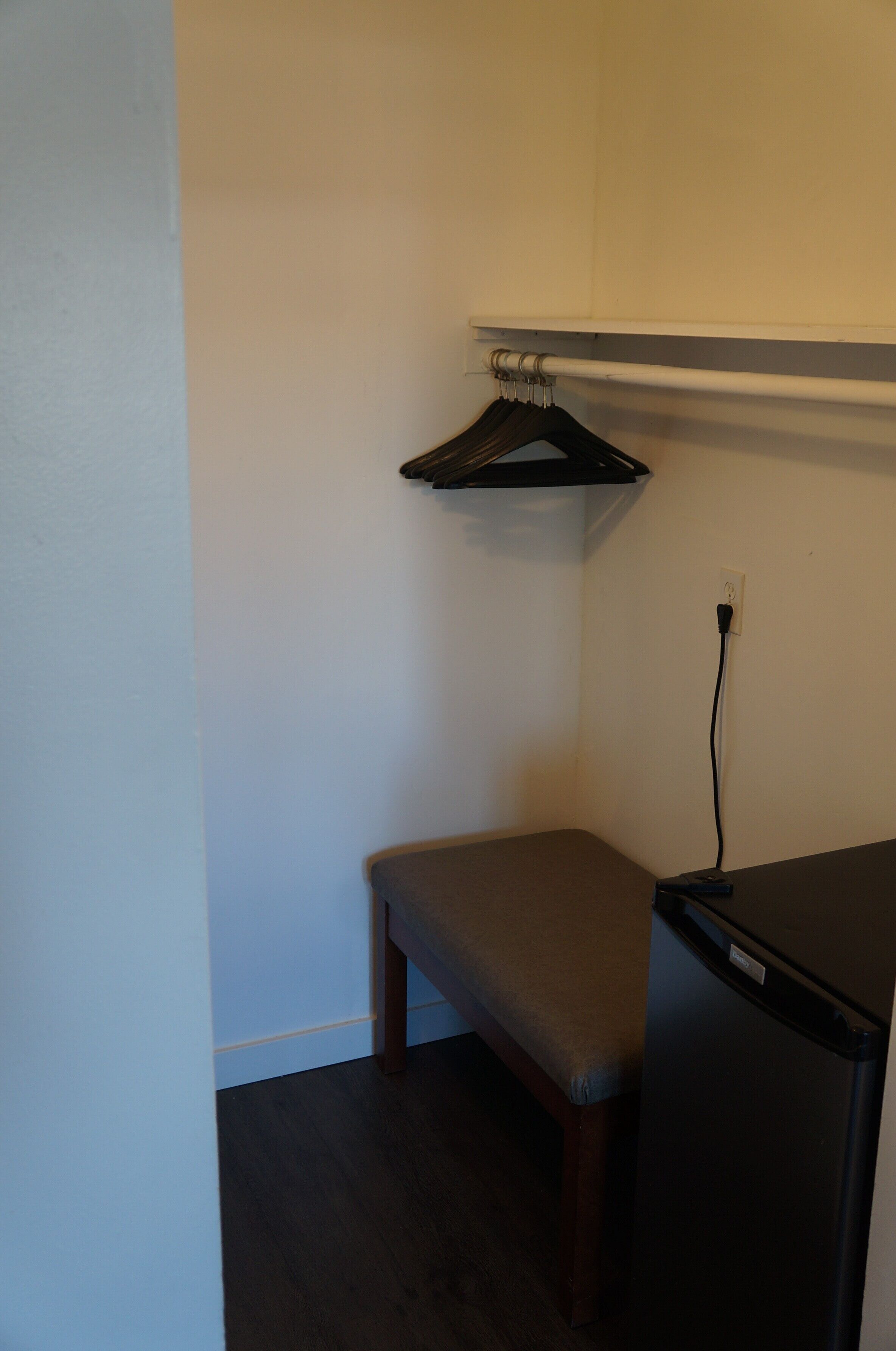 A corner of a room with a bench, a hanging rack, and a refrigerator.