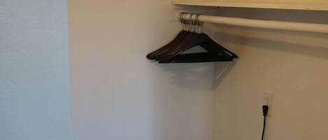 A corner of a room with a bench, a hanging rack, and a refrigerator.