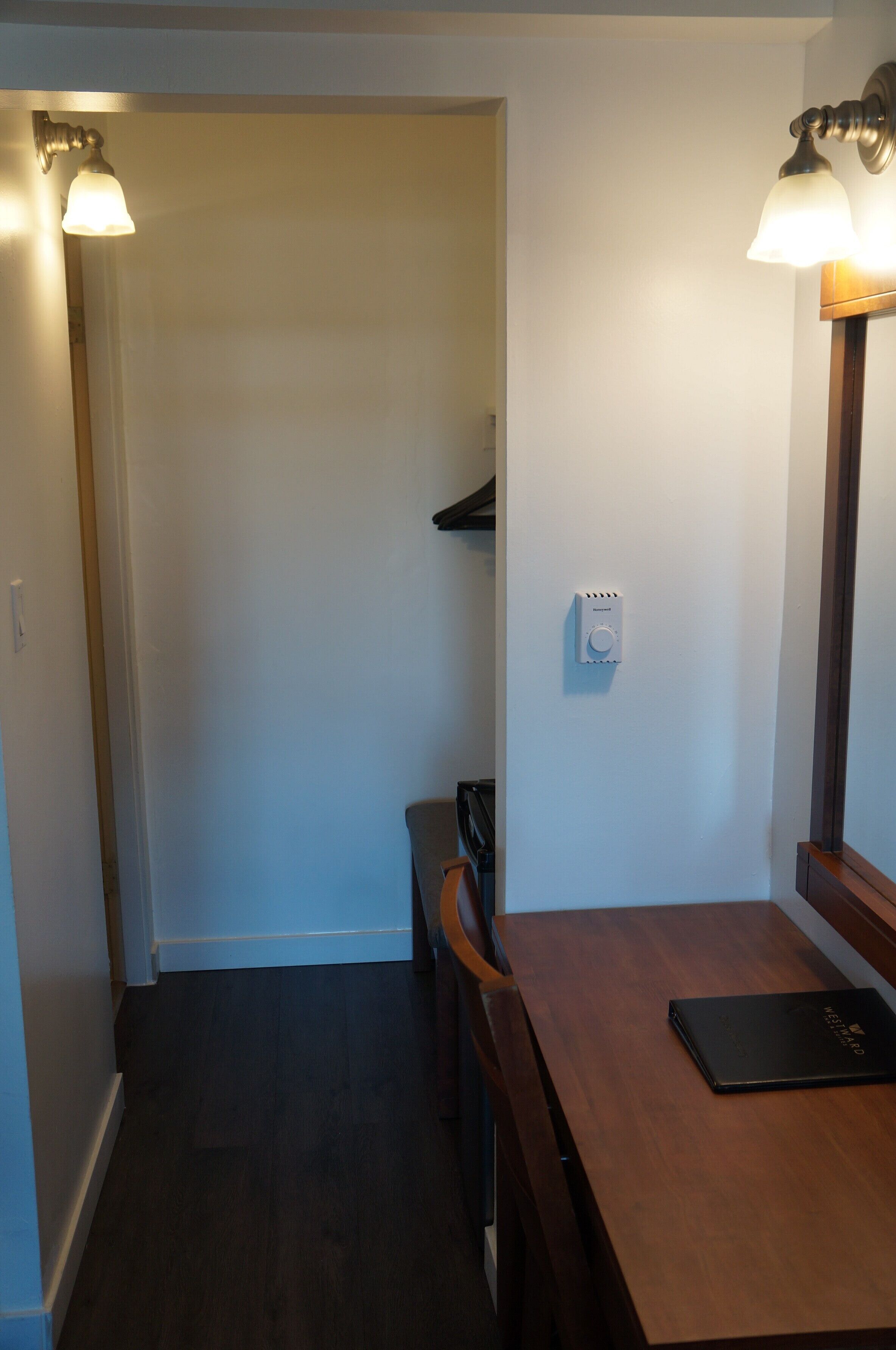 Un pasillo estrecho con una mesa y sillas de madera, un termostato en la pared y dos apliques.