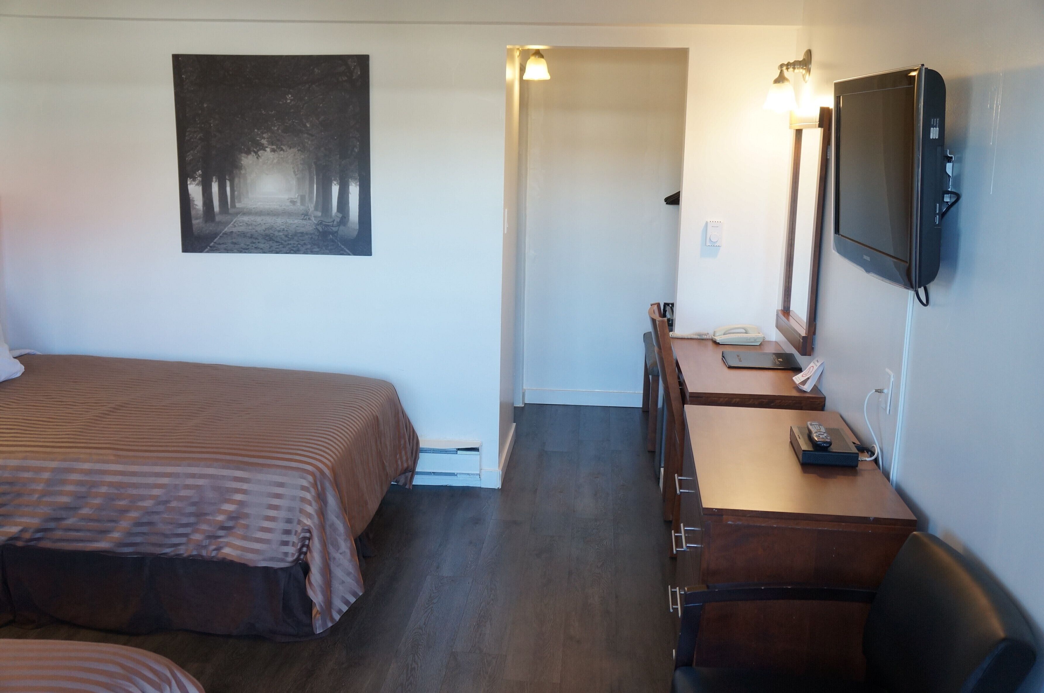 A hotel room with a bed, a desk with a telephone, a mirror, and a wall-mounted television.