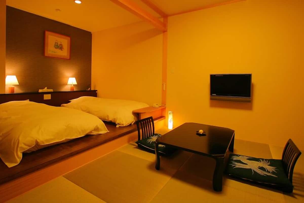 A hotel room with two beds, a small table, chairs, a TV, and a picture on the wall.