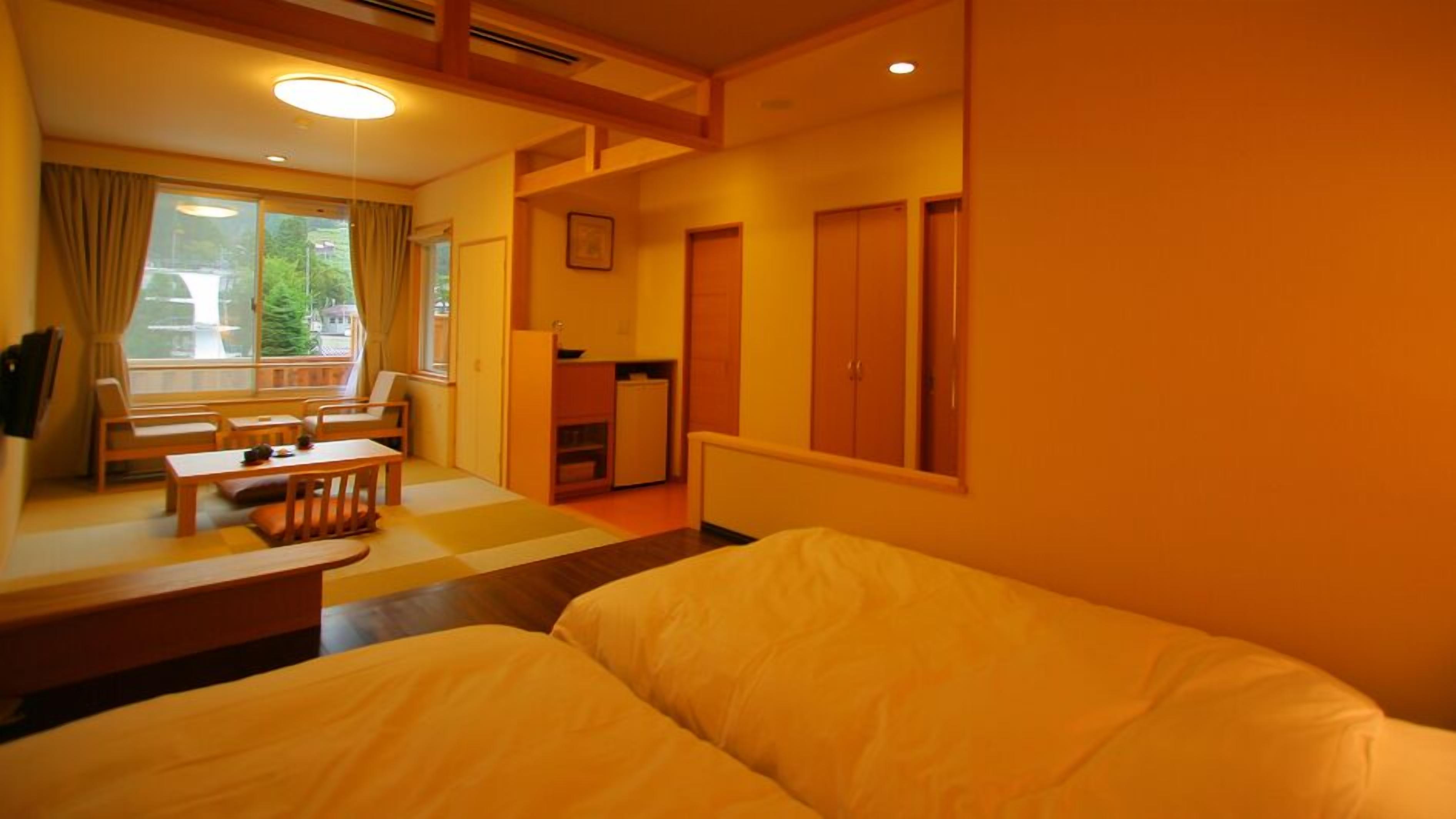 A hotel room with a bed, a small table, chairs, a desk, and a window with curtains.