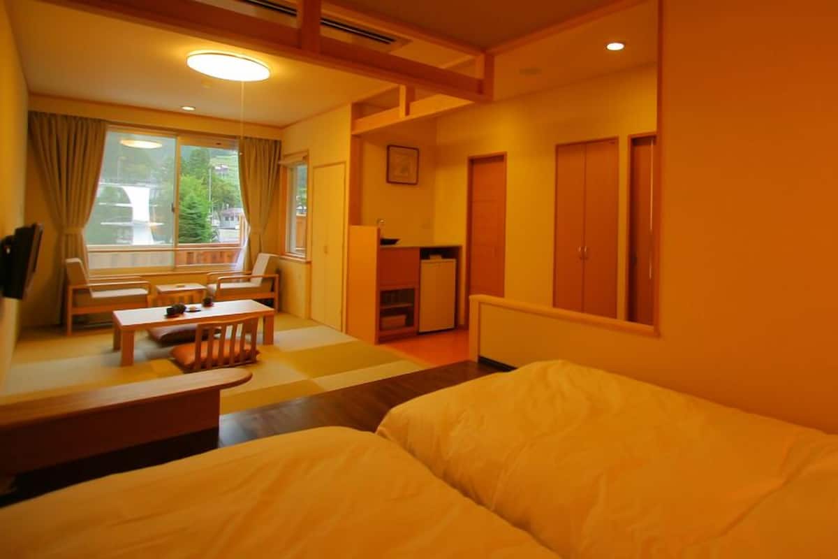 A hotel room with a bed, a small table, chairs, a desk, and a window with curtains.