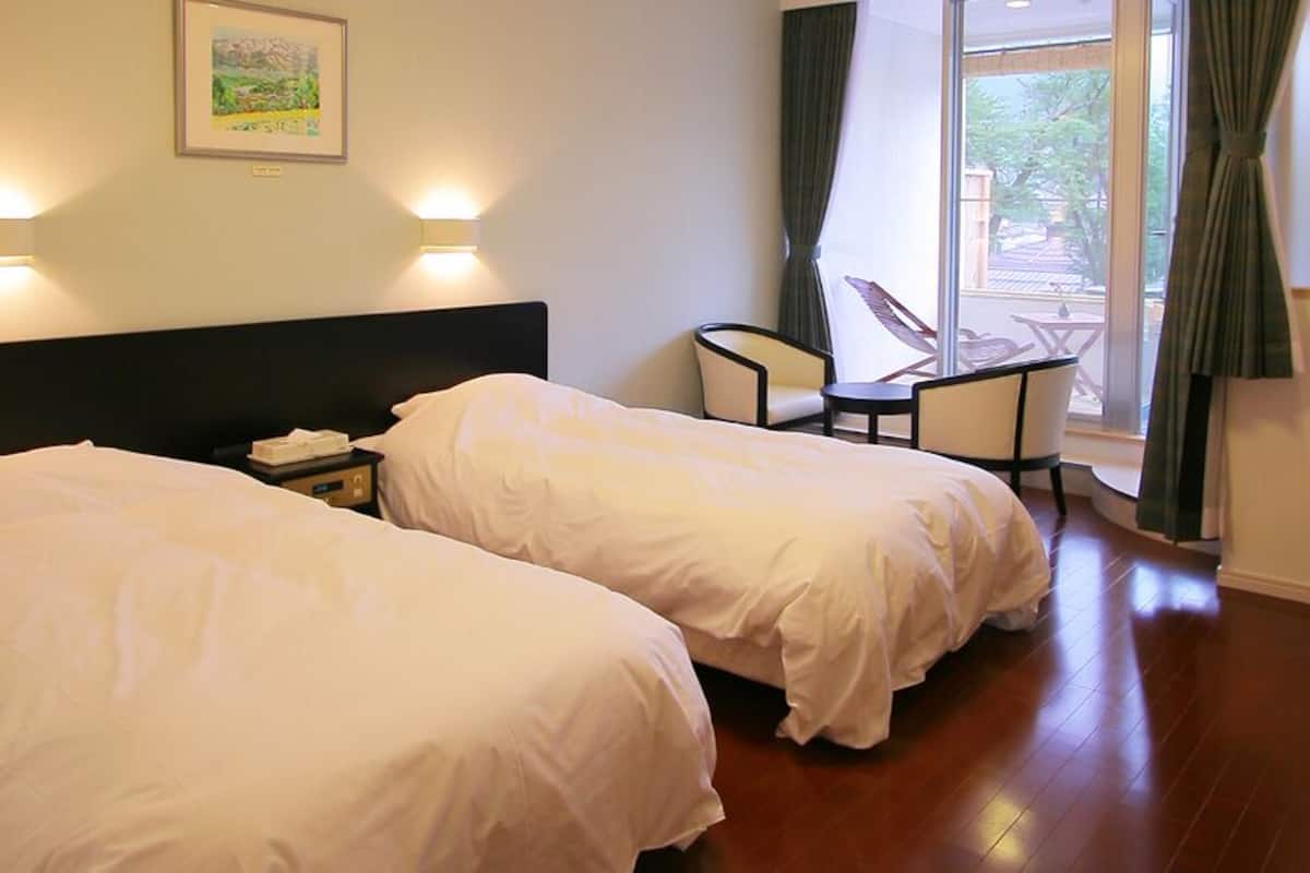 Habitación de hotel con dos camas, un escritorio, una silla y un balcón con vistas.